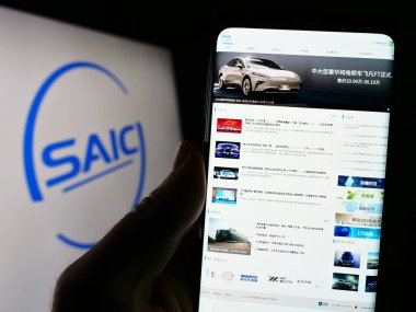 Stuttgart, Almanya - 07-17-2023: Çinli otomotiv şirketi SAIC Motor Corp. Ltd. nin web sitesi ile cep telefonu tutan kişi logolu ekranda. Telefon ekranının merkezine odaklan.