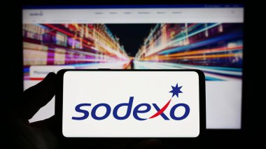 Stuttgart, Almanya - 07-17-2023: Fransız tesis yönetimi şirketi Sodexo S.A. 'nın logosunu elinde tutan kişi web sitesinin önünde ekranda. Telefon ekranına odaklan.