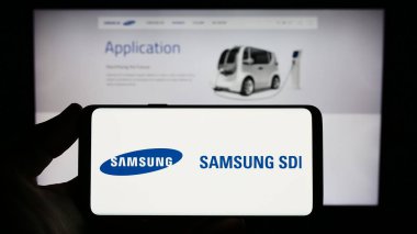 Stuttgart, Germany - 07-17-2023: Person holding smartphone with logo of Korean electronics company Samsung SDI Co. Ltd. on screen in front of website. Focus on phone display. clipart