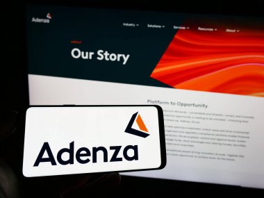 Stuttgart, Almanya - 07-18-2023: Web sayfası önünde ekranda Amerikalı finans yazılım şirketi Adenza Group Inc. 'in logosuyla cep telefonu tutan kişi. Telefon ekranına odaklan.