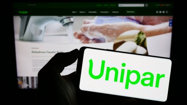 Stuttgart, Germany - 07-18-2023: Person holding cellphone with logo of Brazilian company Unipar Carbocloro S.A. on screen in front of business webpage. Focus on phone display. clipart