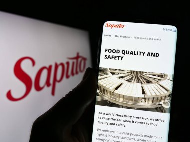 Stuttgart, Almanya - 07-18-2023: Kanadalı mandıra şirketi Saputo Inc. 'nin web sayfası ile logo önünde cep telefonu tutan kişi. Telefon ekranının merkezine odaklan.