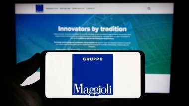Stuttgart, Almanya - 07-18-2023: Bilgi teknolojileri şirketi Maggioli S.P.A. 'nın logosunu elinde tutan kişi web sitesinin önünde ekranda. Telefon ekranına odaklan.