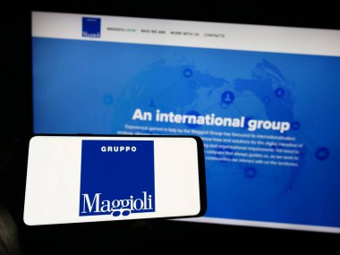 Stuttgart, Germany - 07-18-2023: Person holding mobile phone with logo of information technology company Maggioli S.p.A. on screen in front of web page. Focus on phone display. clipart