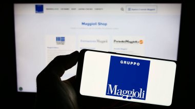 Stuttgart, Almanya - 07-18-2023: Bilgi teknolojisi şirketi Maggioli SpA 'nın logosu olan cep telefonu sahibi kişi iş sayfasının önünde ekranda. Telefon ekranına odaklan.