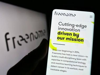 Stuttgart, Almanya - 06-18-2023: ABD 'li biyoteknoloji şirketi Freenome Holding Inc.' in web sayfası ile akıllı telefon sahibi kişi logolu ekranda. Telefon ekranının merkezine odaklan.