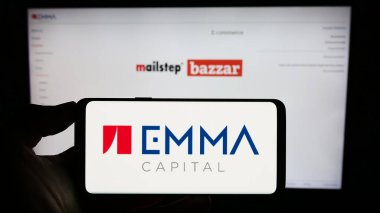 Stuttgart, Almanya - 06-19-2023: Çek yatırım şirketi EMMA Capital 'in logosuna sahip cep telefonu sahibi kişi iş sayfasının önünde ekranda. Telefon ekranına odaklan.