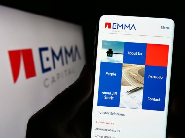 Stuttgart, Almanya - 06-19-2023: Çek yatırım şirketi EMMA Capital 'in web sitesi ile logo önünde cep telefonu tutan kişi. Telefon ekranının merkezine odaklan.