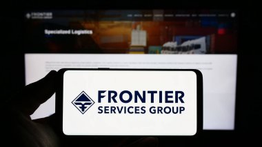 Stuttgart, Almanya - 06-19-2023: İnternet sitesi önünde üzerinde Sınır Hizmetleri Grubu Limited (FSG) logosu bulunan akıllı telefon sahibi kişi. Telefon ekranına odaklan.