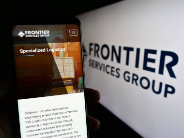 Stuttgart, Almanya - 06-19-2023: Sınır Hizmetleri Grubu Limited (FSG) adlı şirketin internet sayfası ile cep telefonu tutan kişi logolu ekranda. Telefon ekranının merkezine odaklan.