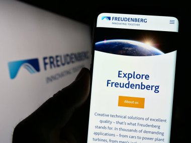 Stuttgart, Almanya - 06-19-2023: Alman firması Freudenberg SE 'nin web sitesi ile cep telefonu sahibi kişi iş logosu önünde ekranda. Telefon ekranının merkezine odaklan.