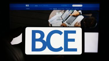 Stuttgart, Germany - 06-23-2023: Person holding smartphone with logo of Canadian telecommunications company BCE Inc. on screen in front of website. Focus on phone display. clipart