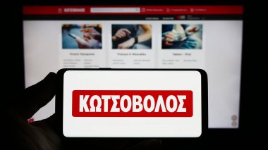 Stuttgart, Almanya - 06-24-2023: Yunan elektronik perakende şirketi Kotsovolos 'un logosuna sahip akıllı telefon sahibi kişi web sitesi önünde ekranda. Telefon ekranına odaklan.