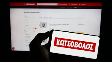 Stuttgart, Almanya - 06-24-2023: Yunan elektronik perakende şirketi Kotsovolos 'un logosunun bulunduğu cep telefonu sahibi kişi iş sayfası önünde ekranda. Telefon ekranına odaklan.
