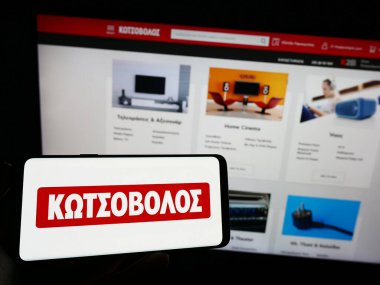 Stuttgart, Almanya - 06-24-2023: Yunan elektronik perakende şirketi Kotsovolos 'un logosuna sahip cep telefonu sahibi kişi web sayfasının önünde ekranda. Telefon ekranına odaklan.