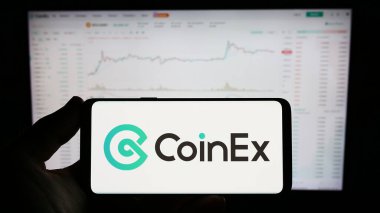 Stuttgart, Almanya - 06-24-2023: Kripto döviz şirketi CoinEx 'in logosu olan cep telefonu sahibi kişi iş sayfasının önünde ekranda. Telefon ekranına odaklan.