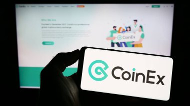 Stuttgart, Almanya - 06-24-2023: Kripto döviz şirketi CoinEx 'in logosu olan cep telefonu sahibi kişi iş sayfasının önünde ekranda. Telefon ekranına odaklan.