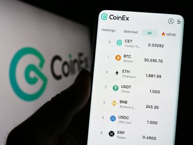 Stuttgart, Almanya - 06-24-2023: Şifreleme döviz şirketi CoinEx 'in web sayfası olan akıllı telefonu logo önünde ekranda tutan kişi. Telefon ekranının merkezine odaklan.