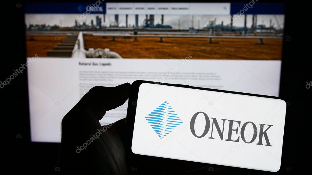 Stuttgart, Germany - 06-18-2023: Person holding mobile phone with logo of American natural gas company Oneok Inc. on screen in front of business web page. Focus on phone display.