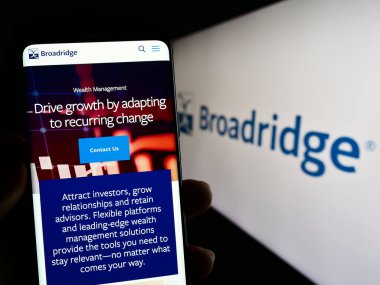 Stuttgart, Almanya - 06-24-2023: ABD 'li Broadridge Financial Solutions Inc.' in web sayfası ile akıllı telefon sahibi kişi logo ile ekranda. Telefon ekranının merkezine odaklan.