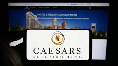 Stuttgart, Almanya - 06-24-2023: ABD 'li Caesars Entertainment Inc. şirketinin logosunu elinde tutan kişi web sitesinin önünde ekranda. Telefon ekranına odaklan.