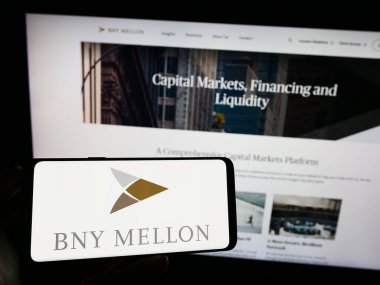 Stuttgart, Germany - 06-24-2023: Person holding cellphone with logo of The Bank of New York Mellon Corporation (BNY) on screen in front of webpage. Focus on phone display. clipart