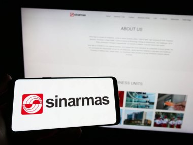 Stuttgart, Almanya - 04-23-2023: Endonezya holdingi Sinar Mas Group 'un logosunun bulunduğu akıllı telefonu web sitesinin önünde tutan kişi. Telefon ekranına odaklan.