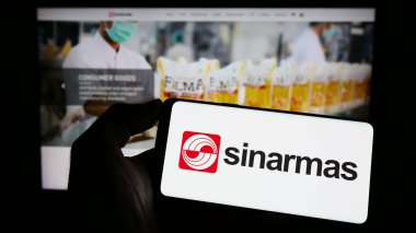 Stuttgart, Almanya - 04-23-2023: Endonezya holdingi Sinar Mas Group 'un logosunun bulunduğu cep telefonu sahibi kişi iş sayfasının önünde ekranda. Telefon ekranına odaklan.