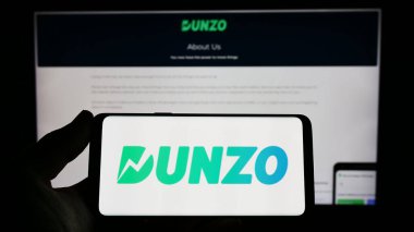 Stuttgart, Almanya - 04-23-2023: Hintli dağıtım uygulaması şirketi Dunzo Digital 'in logosunu elinde tutan kişi web sitesinin önünde ekranda. Telefon ekranına odaklan.