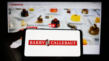 Stuttgart, Germany - 04-24-2023: Person holding cellphone with logo of Swiss chocolate company Barry Callebaut AG on screen in front of business webpage. Focus on phone display. clipart