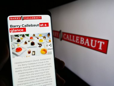Stuttgart, Almanya - 04-24-2023: İsviçreli çikolata şirketi Barry Callebaut AG 'nin internet sayfası ile akıllı telefon taşıyan kişi ekranda logolu. Telefon ekranının merkezine odaklan.