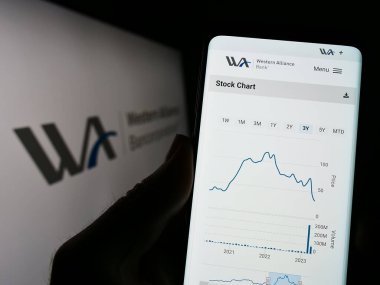 Stuttgart, Almanya - 04-24-2023: ABD 'li Western Alliance Bancorporation şirketinin web sitesi ile logo önünde cep telefonu tutan kişi. Telefon ekranının merkezine odaklan.