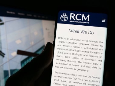 Stuttgart, Germany - 04-24-2023: Person holding cellphone with web page and logo of company Rokos Capital Management LLP (RCM) on screen. Focus on center of phone display. clipart