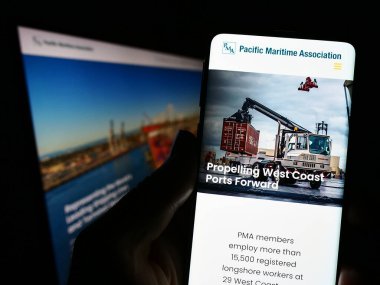 Stuttgart, Almanya - 04-25-2023: Ekranda Pacific Maritime Association (PMA) organizasyonunun web sayfası ve logosuna sahip cep telefonu tutan kişi. Telefon ekranının merkezine odaklan.