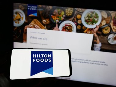 Stuttgart, Almanya - 04-25-2023: İngiliz Hilton Food Group plc şirketinin logosuyla cep telefonu sahibi kişi iş sayfasının önünde ekranda. Telefon ekranına odaklan.