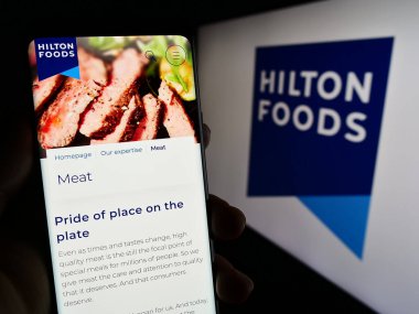 Stuttgart, Almanya - 04-25-2023: İngiliz Hilton Food Group plc şirketinin web sayfası olan akıllı telefon sahibi kişi logonun önünde ekranda. Telefon ekranının merkezine odaklan.