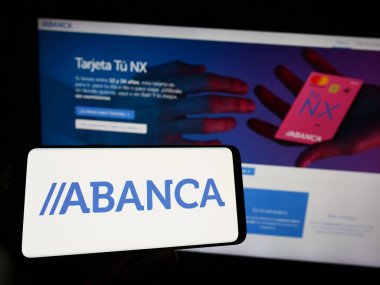 Stuttgart, Almanya - 04-26-2023: ABANCA Corporacion Bancaria S.A. şirketinin logosuna sahip cep telefonu sahibi kişi iş sayfasının önünde ekranda. Telefon ekranına odaklan.