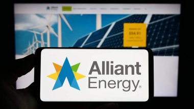 Stuttgart, Almanya - 04-26-2023: ABD 'li Alliant Energy Corporation şirketinin logosuyla cep telefonu sahibi kişi iş sayfasının önünde ekranda. Telefon ekranına odaklan.