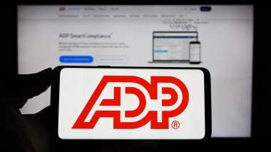 Stuttgart, Almanya - 04-26-2023: Web sitesi önünde ABD 'li Automatic Data Processing Inc. (ADP) şirketinin logosuna sahip akıllı telefon sahibi kişi. Telefon ekranına odaklan.
