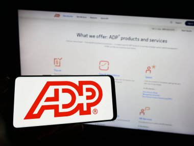Stuttgart, Almanya - 04-26-2023: Web sayfası önünde üzerinde Amerikan şirketi Automatic Data Processing Inc. (ADP) logosu bulunan cep telefonu sahibi kişi. Telefon ekranına odaklan.