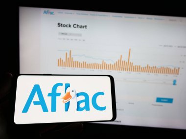Stuttgart, Almanya - 04-26-2023: Amerikan sigorta şirketi Aflac Inc. 'in logosunun bulunduğu cep telefonu sahibi kişi iş sayfasının önünde ekranda. Telefon ekranına odaklan.