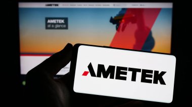 Stuttgart, Germany - 04-27-2023: Person holding smartphone with logo of US electronics company AMETEK Inc. on screen in front of website. Focus on phone display. clipart