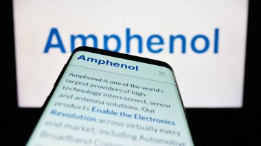 Stuttgart, Germany - 04-27-2023: Mobile phone with webpage of US electronics company Amphenol Corporation on screen in front of business logo. Focus on top-left of phone display. clipart