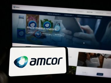 Stuttgart, Almanya - 04-27-2023: Amcor plc ambalaj şirketinin logosuna sahip cep telefonu sahibi kişi iş sayfasının önünde ekranda. Telefon ekranına odaklan.