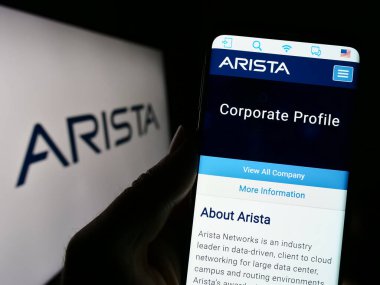 Stuttgart, Germany - 04-28-2023: Person holding cellphone with webpage of computer networking company Arista Networks Inc. on screen with logo. Focus on center of phone display. clipart