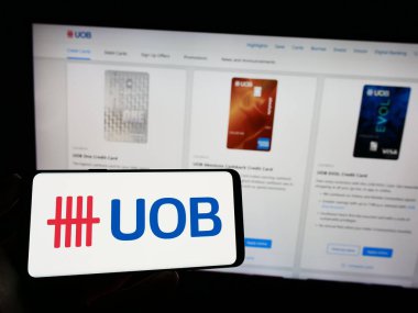 Stuttgart, Almanya - 04-28-2023: Birleşik Denizaşırı Banka Limited (UOB) şirketinin logosuyla cep telefonu sahibi kişi iş sayfası önünde ekranda. Telefon ekranına odaklan.
