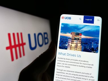 Stuttgart, Almanya - 04-28-2023: Logo önündeki ekranda United Overseas Bank Limited (UOB) şirketinin web sayfası bulunan kişi. Telefon ekranının merkezine odaklan.