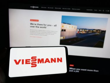 Stuttgart, Almanya - 04-28-2023: Alman şirketi Viessmann Group GmbH Co. KG 'nin logosuyla cep telefonu sahibi olan kişi iş sayfası önünde ekranda. Telefon ekranına odaklan.