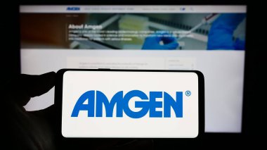 Stuttgart, Almanya - 06-17-2023: ABD 'li biyofarmasötik şirketi Amgen Inc.' in logosunu elinde tutan kişi web sitesinin önünde ekranda. Telefon ekranına odaklan.