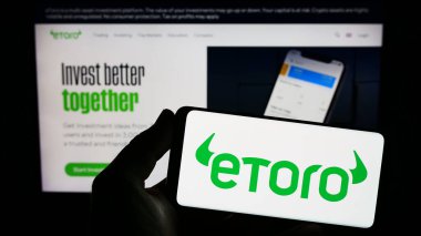 Stuttgart, Almanya - 06-17-2023: İsrailli sosyal ticaret şirketi eToro 'nun logosunu elinde tutan kişi web sitesinin önünde ekranda. Telefon ekranına odaklan.
